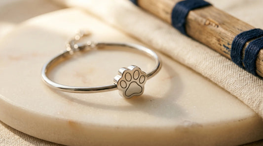 A polished 316L stainless steel paw-print bracelet resting on pale stone in warm daylight