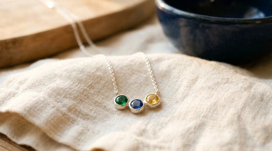 A small pendant with three birthstones in an arc layout against cream linen