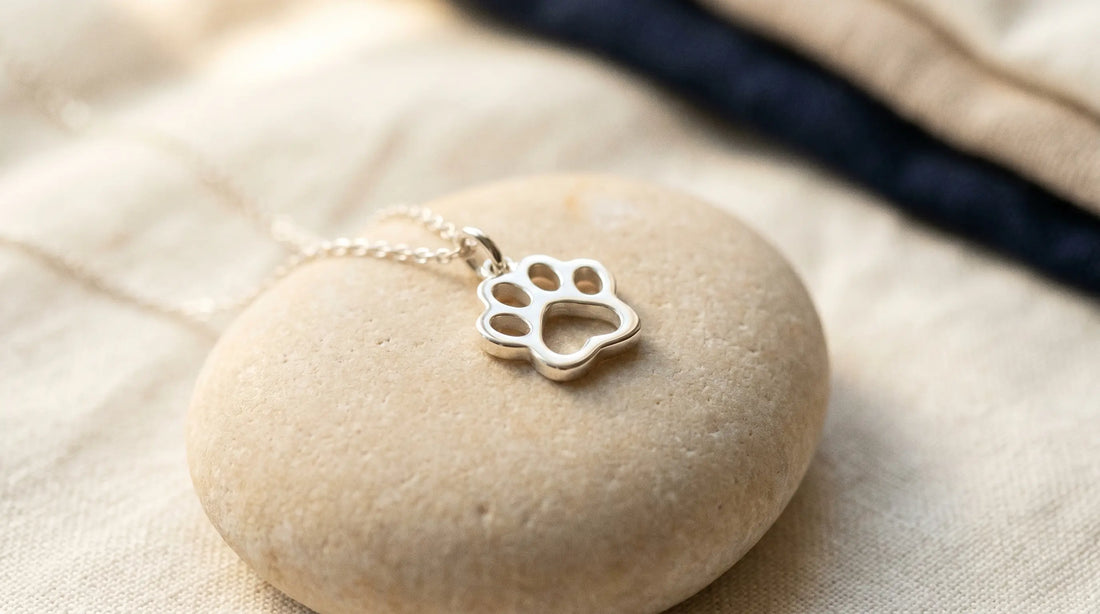 A small cat paw silhouette pendant resting on pale stone in soft daylight