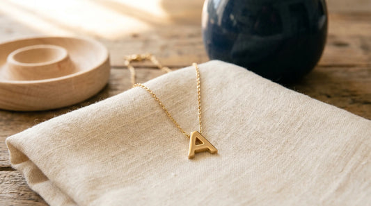 A small sans-serif initial 'A' pendant on a fine cable chain against warm cream linen