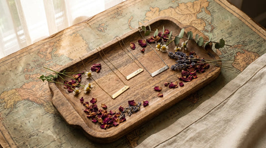Personalized necklaces arranged on a vintage world map with dried flowers from different regions in overhead light