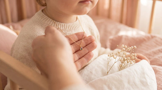 Mother's hand clasping a delicate birthstone pendant necklace on a small child in soft pastel light