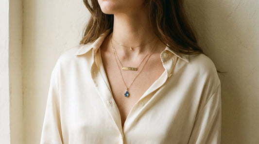 Three layered personalized necklaces of varying lengths styled on a cream silk blouse in natural light
