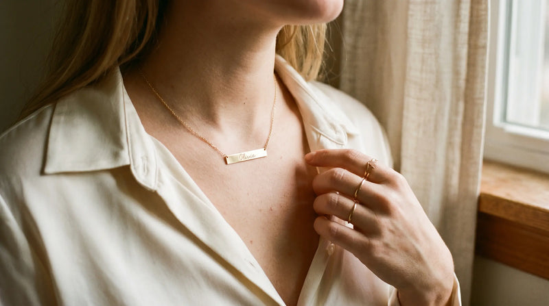 Sideways gold-plated name necklace lying flat across collarbone — modern minimalist style